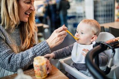 Foster carer feeding baby Woman foster carer smiling and feeding a baby in a high chair