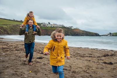 Man on beach with young boy on shoulders and young boy running in front of him Man on beach with young boy on shoulders and young boy running in front of him