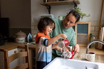 Boy washing dishes with man