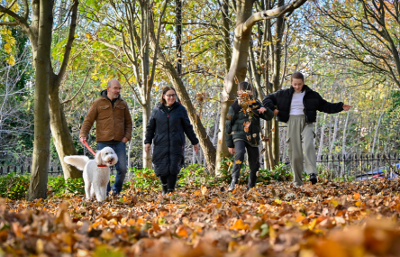 Family of four walking with a dog and kicking leaves